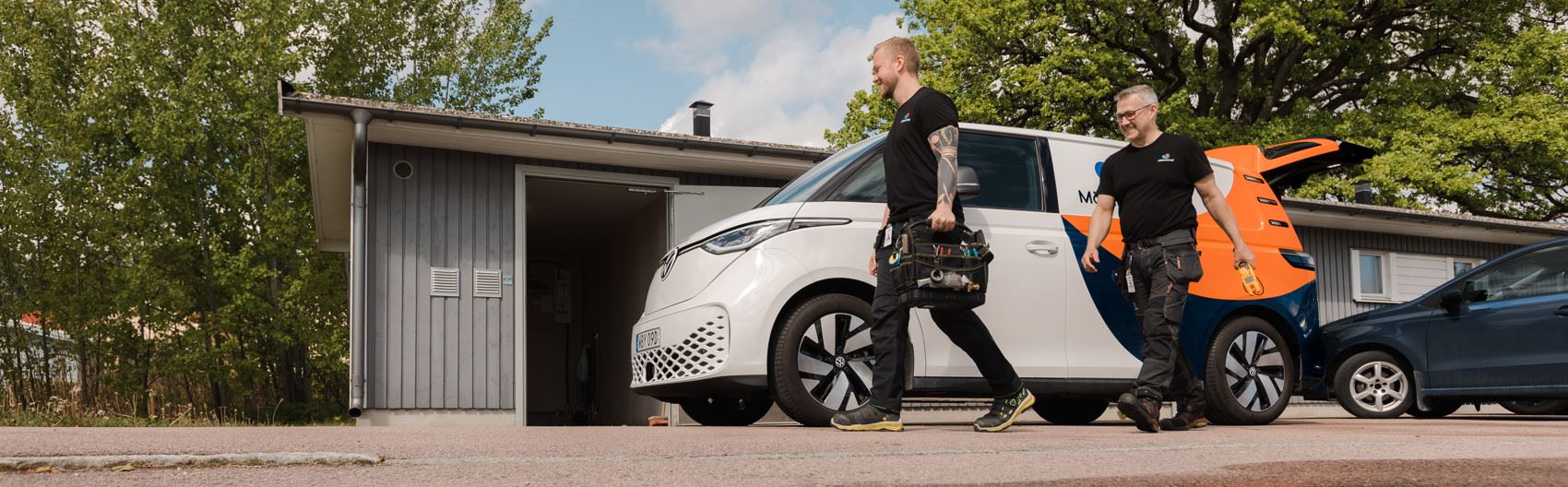 Två personer går med en verktygsväska mot ett hus.