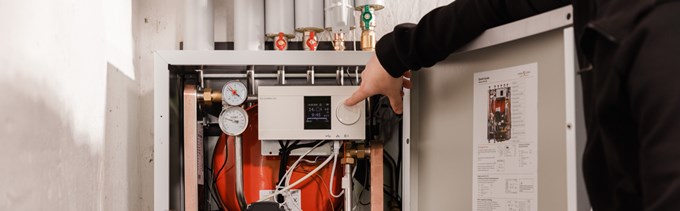 En hand pekar in i en fjärrvärmecentral. Runt om syns olika rör.