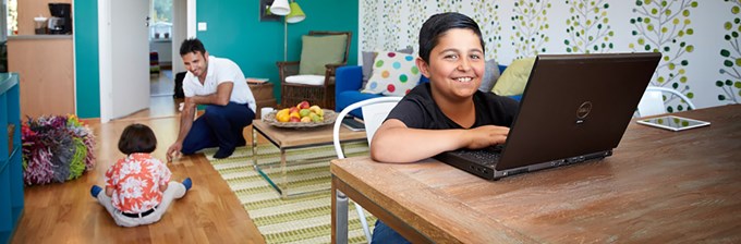 Barn sitter framför en dator medan familjen leker i bakgrunden